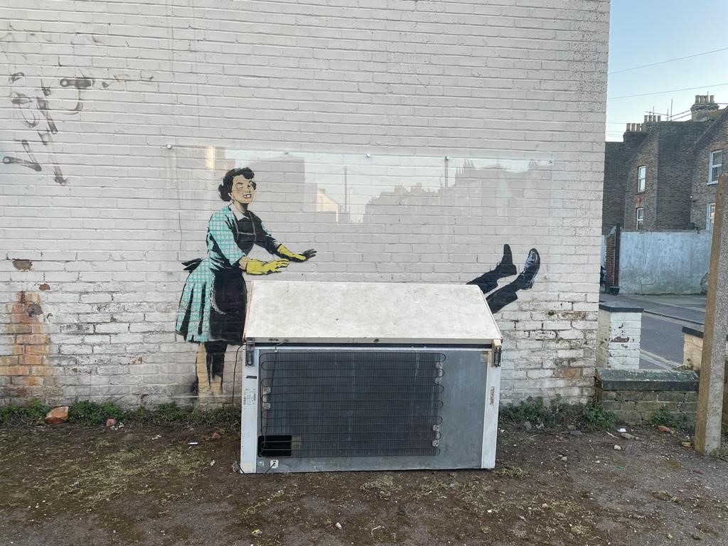 We used a sheet of clear perspex to give an immediate solution to  protect the Banksy. It was shaped to insure the rain didn't damage the art work.