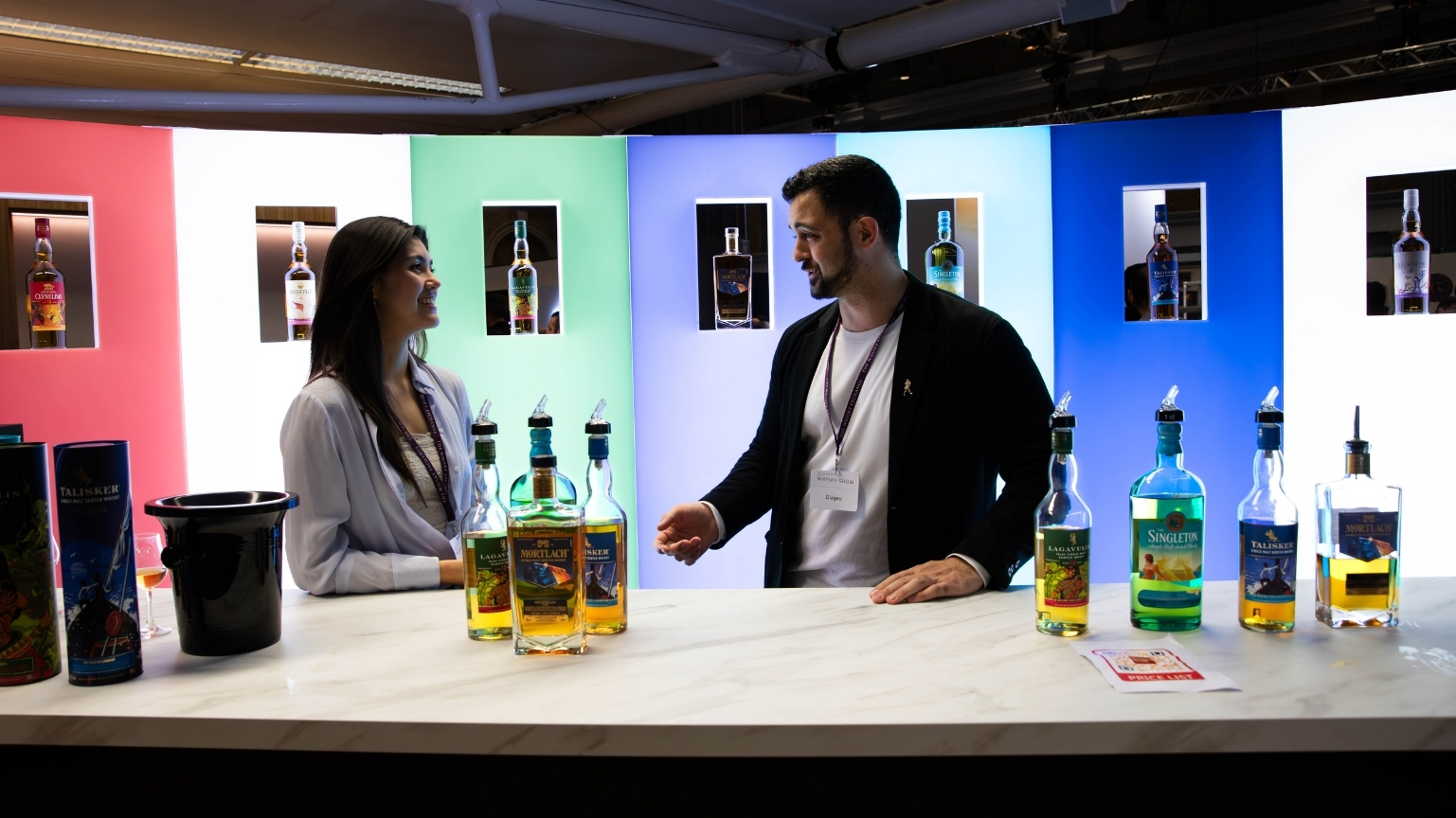 Photograph taken at an exhibition showing people in the foreground promoting whisky and the led lit, curved display wall in the background wghich we fabricated.